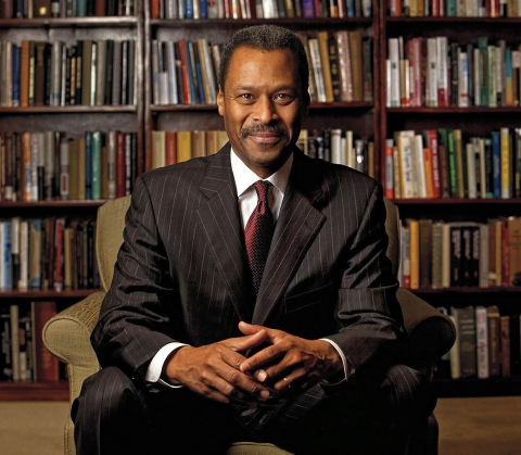 John Silvanus Wilson Jr. smiling and sitting in front of a bookshelf